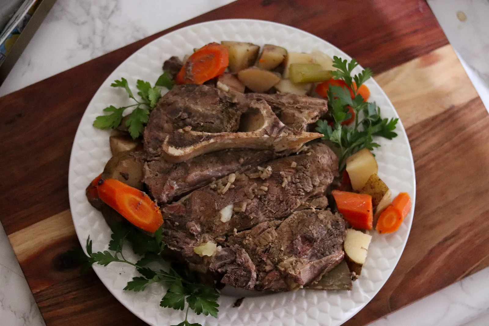Barton Beef roast with carrots, potatoes and fresh parsley, plated on a cutting board